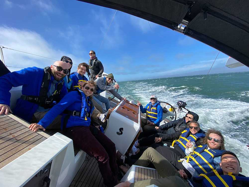 A team of Digital Foundry software engineers, designers and software consultants ride on the deck of a sailboat in San Francisco bay. The sailboat is leaning at an extreme angle in strong wind.