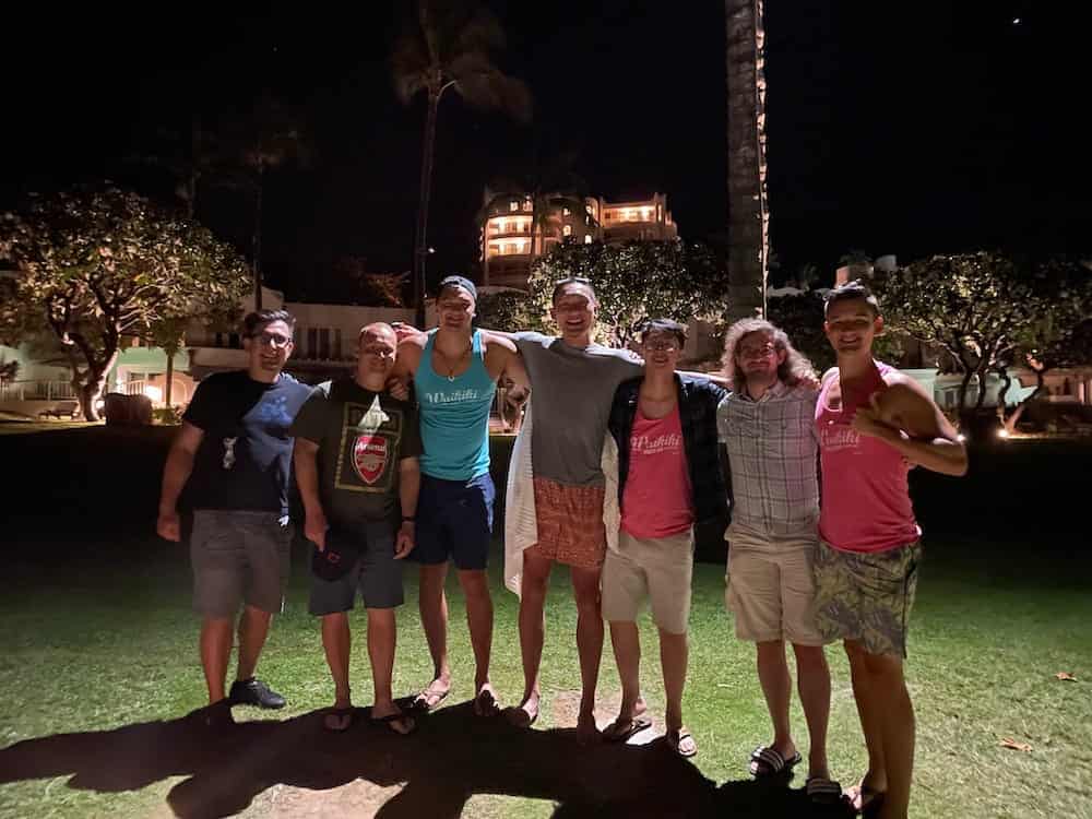 A group of seven digital foundry software engineers and software consultants stand together on a lawn in front of a resort hotel in Hawaii at night, arms over each other's shoulders
