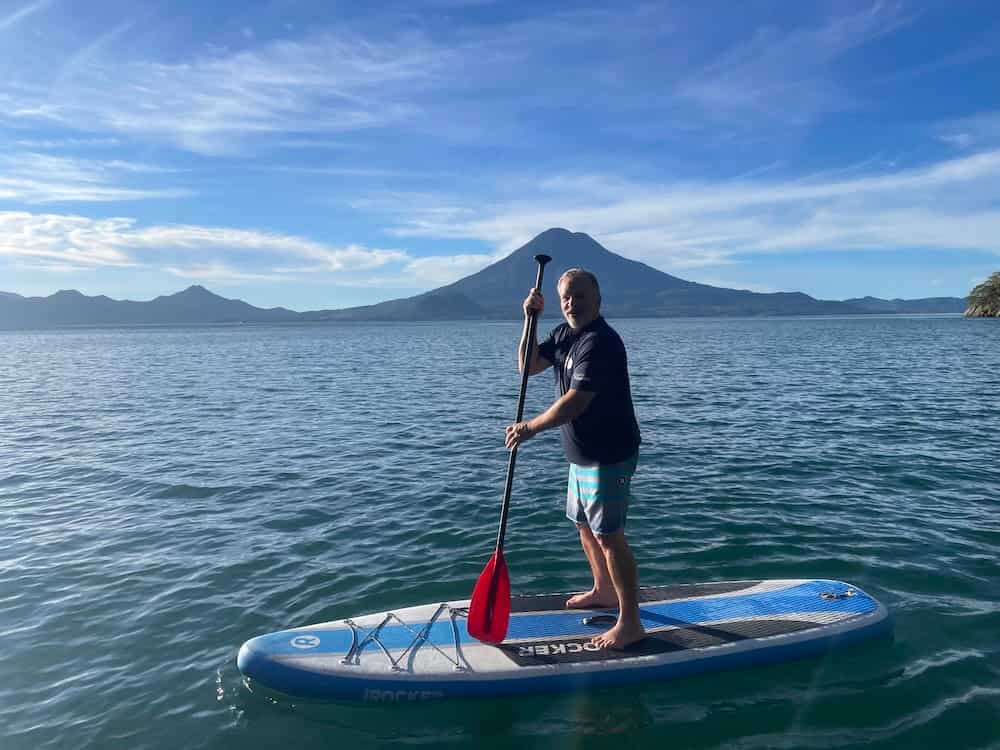 A digital foundry employee stands on a stand-up paddleboard on lake Atitlan, with volcanos in the background