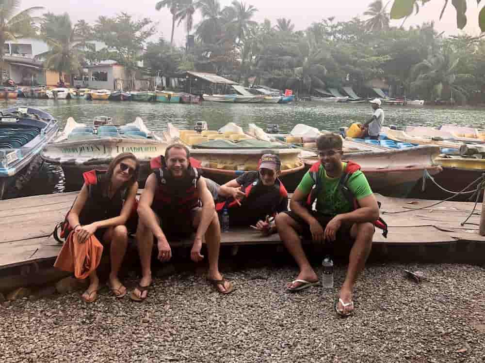 Four Digital Foundry software consultants wearing life vests sit on a deck alongside a river with boats tied up to the bank in Sri Lanka