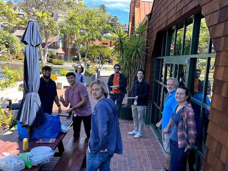 A group of digital foundry software engineers, software consultants, UX designers and software architects stand on the brick patio outside the digital foundry office at lunch while pizza is cooking